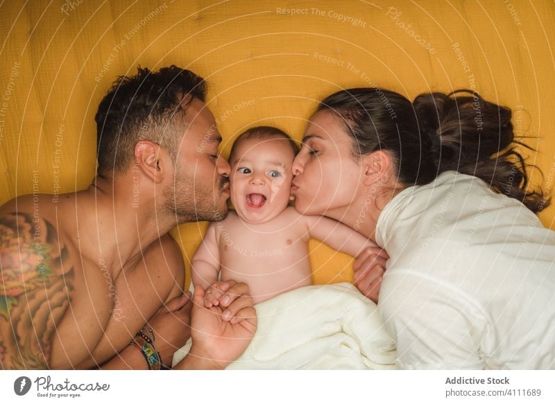 Mother and father kissing baby mother together hug family embrace love lying bed happy child adorable cute kid little care parent relax bonding home comfort