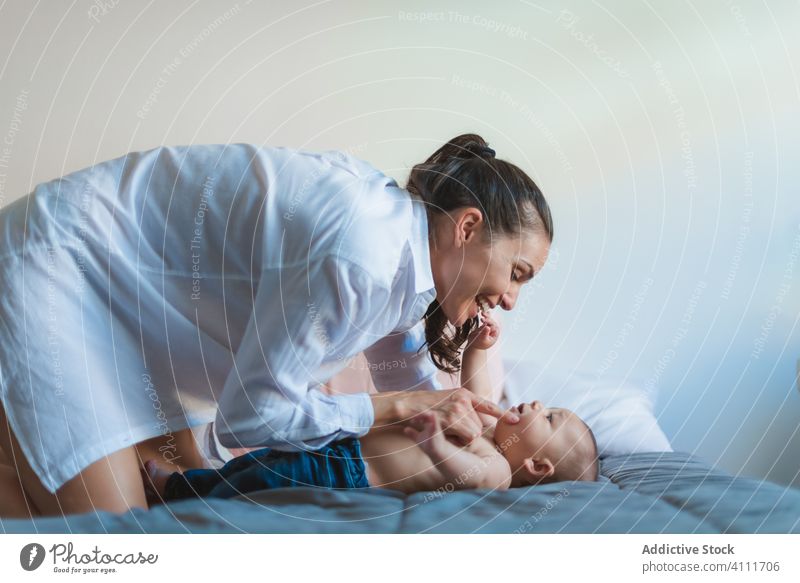 Overjoyed mother and happy little baby on bed lying smile laugh enjoy play together love home care parent child tender infant lifestyle comfort innocent