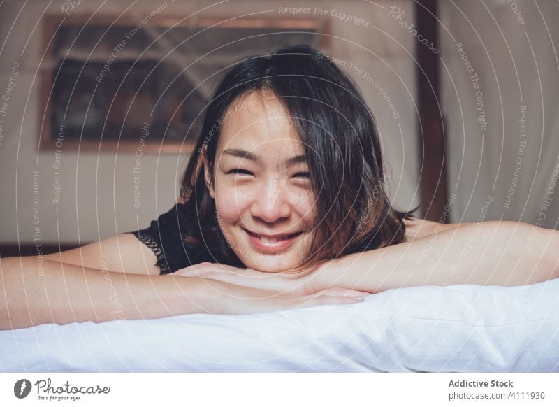 Happy ethnic woman lying on bed home laugh morning relax bedroom comfort female rest weekend cheerful cozy affection young joy lifestyle pillow lazy giggle lady
