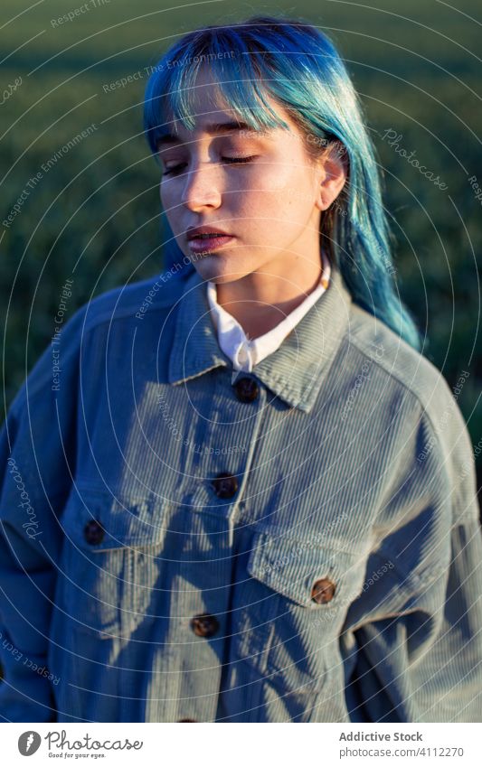 Sad stylish woman standing in field trendy melancholy pensive sad informal dyed hair alone hipster blue hair style fashion calm sunlight young meadow evening