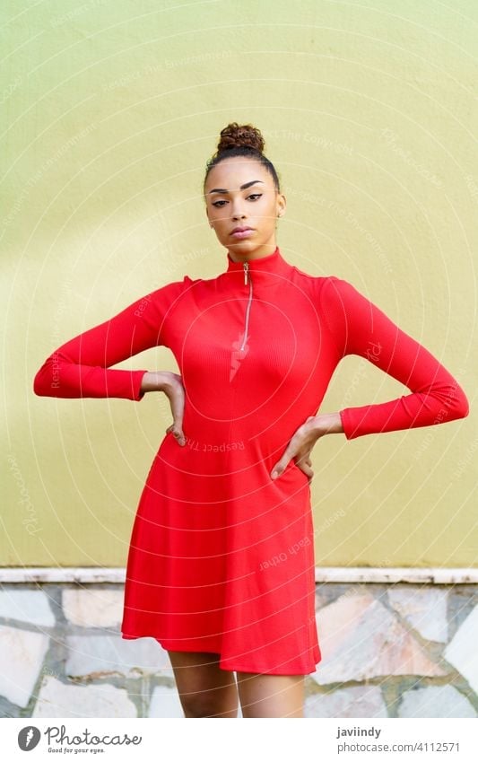 Young black woman in red dress with a serious expression in urban background. bow hairstyle model beauty fashion pretty portrait girl young female person lady