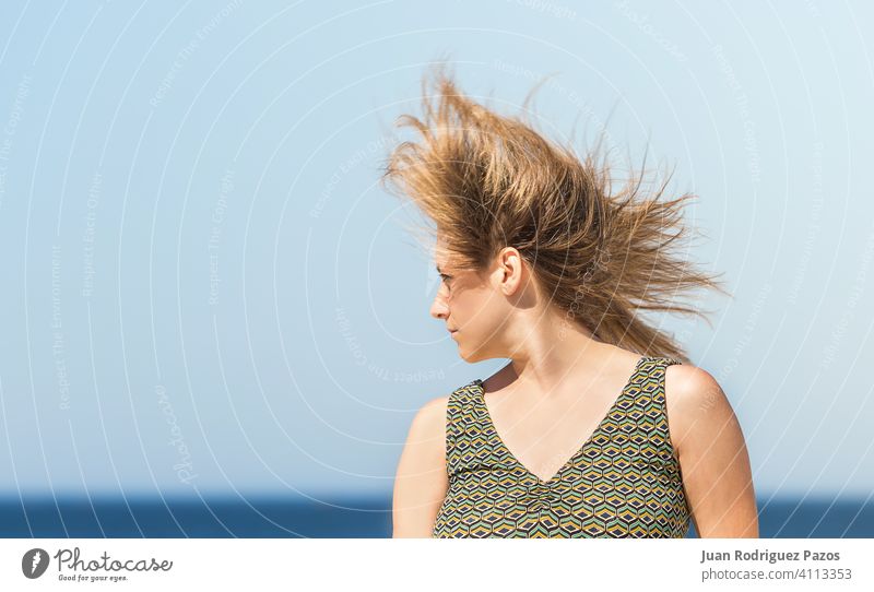 Portrait of a middle-aged blonde caucasian woman in a green dress and hair shaking in the wind sea summer sun relax outdoor female lady sunny alone outside