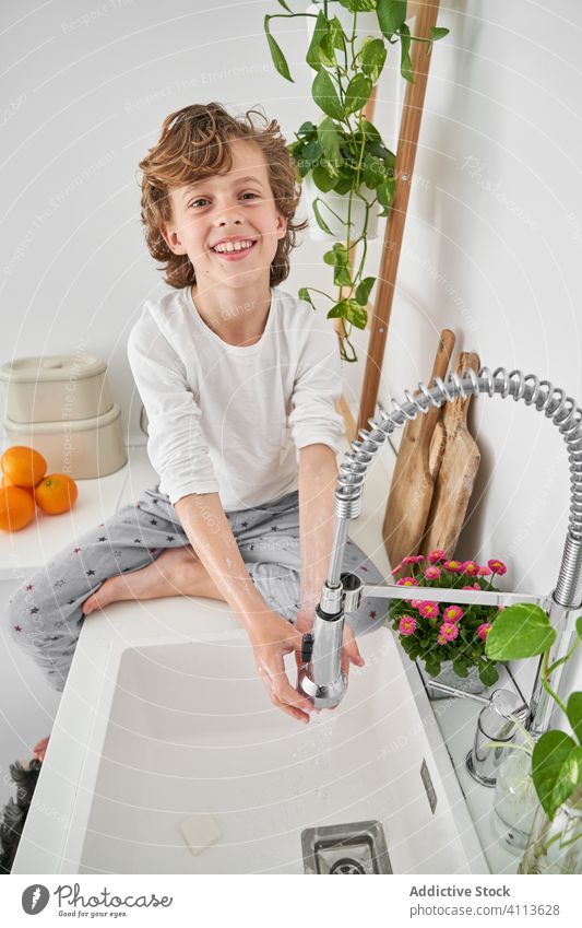 Blond child washing his hands in the kitchen sink to prevent any infection lifestyle kid indoors son boy water home young hygiene domestic childhood folding