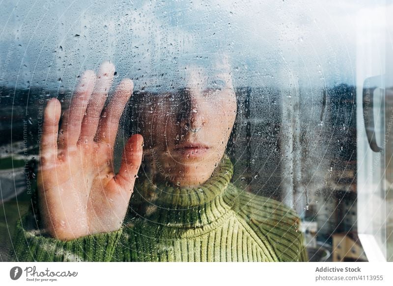 Melancholic young woman looking through window sad depression isolation coronavirus home desperate lonely unhappy female wet rain melancholy solitude stress