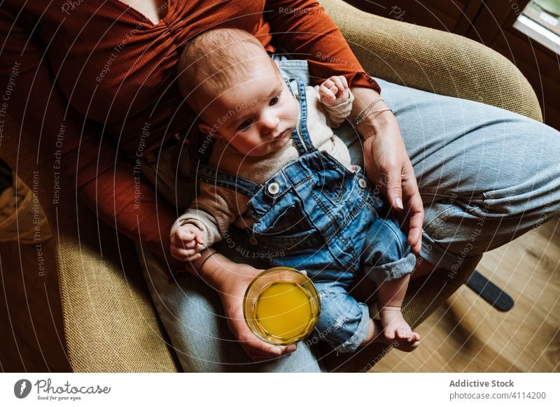 Crop mother with juice and baby resting on chair healthy cozy sit love home tender woman fresh drink beverage adorable child kid infant room together parent