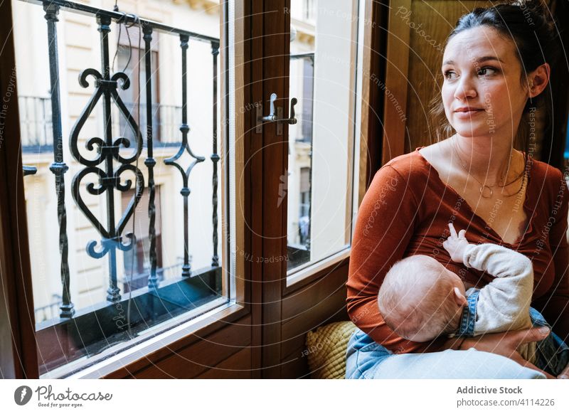 Happy mother breastfeeding baby near window home happy love rest cozy sit woman cute room hug embrace smile child kid childhood little care together parent