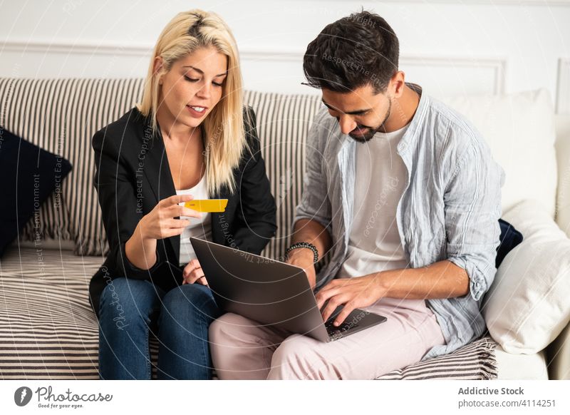Happy diverse couple shopping online on couch laptop credit card together sofa home smile man woman credential store buy transfer money finance multiethnic