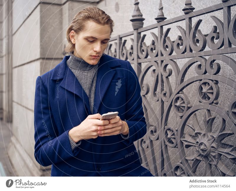 Stylish young man browsing on smartphone on street talk city style trendy elegant serious pensive urban metrosexual device gadget conversation modern lifestyle