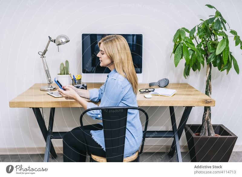 Blonde woman working at home desk smartphone mobile phone communication device businesswoman indoor table female laptop desktop computer design lifestyle office