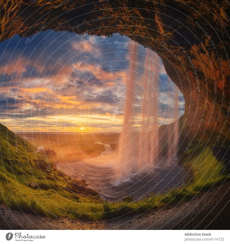 Cave with waterfall during sunset cave sea shore entrance cloudy sky iceland evening majestic grass stone cascade sundown moss ocean landscape nature rough