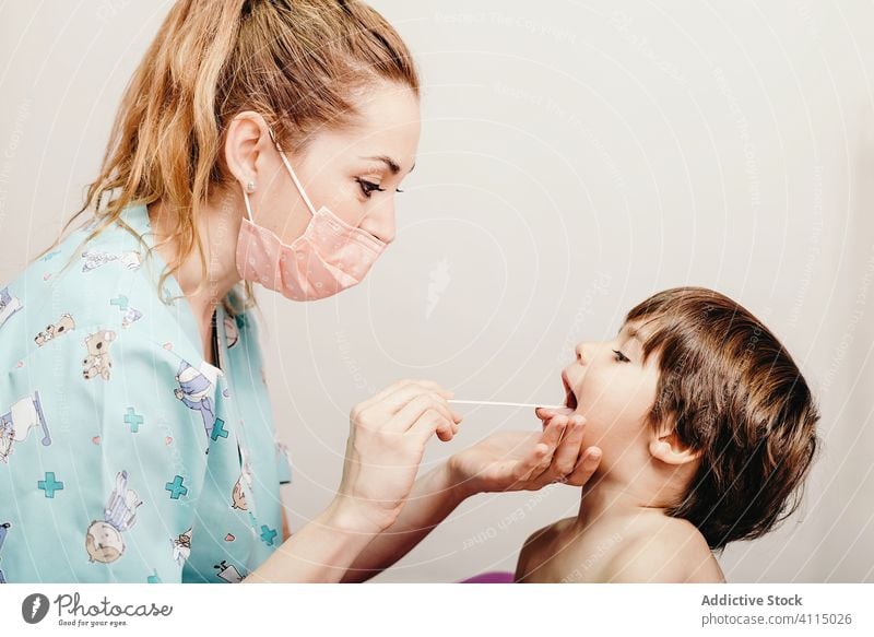Pediatrician examining throat of little patient child doctor examine clinic boy nurse woman mouth opened hospital respiratory kid specialist health care