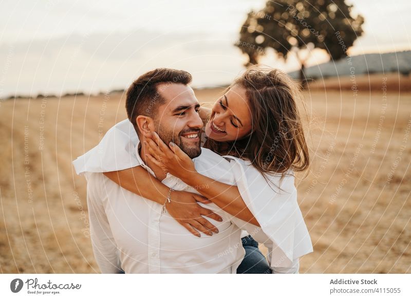 Delighted couple having fun in field piggyback date evening happy love ride man woman relationship together meadow dry romantic girlfriend boyfriend lifestyle