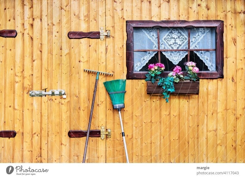 A garden hut with window, curtain, flower box, broom and rake leaning in front of it. Gardening garden shed Window flowers Window box Broom Rake