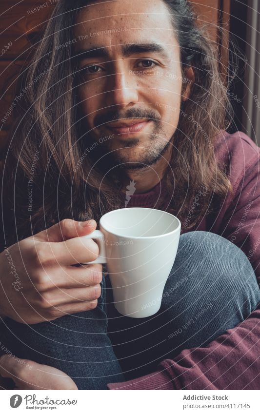 Bearded man resting with hot beverage drink home stay at home coronavirus covid-19 cozy mug mood adult room male relax tea coffee cup comfort long hair beard