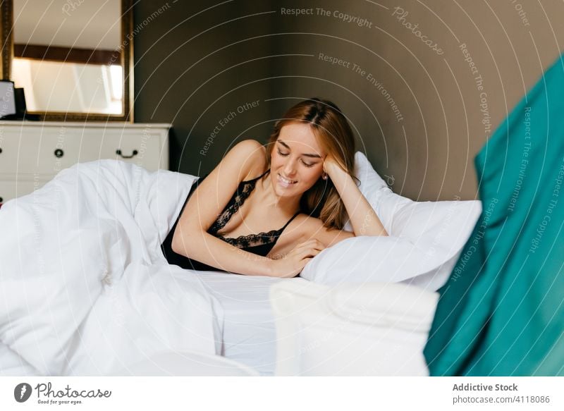 Seductive young brown-haired woman in white bra and panties lying down on  bed at home.. Stock Photo