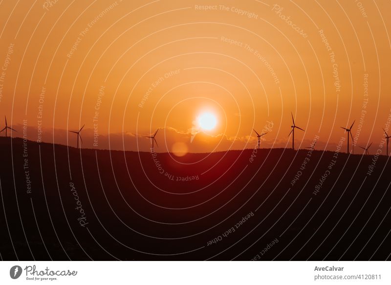Silhouettes of some wind mills on the top of a mountain during a super orange sunset with copy space peaceful windmill plant energy renewable industrial