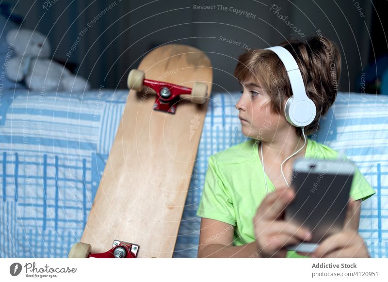Cheerful kid with headphones using smartphone at home gadget boy chat child device online listen internet happy lifestyle modern mobile connection digital
