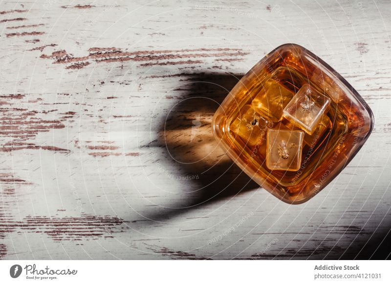 Glass of scotch in rays on aged rustic table in darkness glass whiskey bourbon alcohol beverage ice drink liquid liquor cognac brandy transparent fluid pour