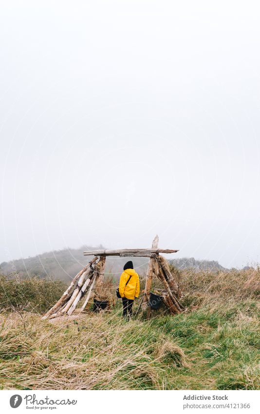 Female traveler beside wooden construction in misty countryside woman fog tourism alone lost trip solitude raincoat adventure hike explore female foggy yellow