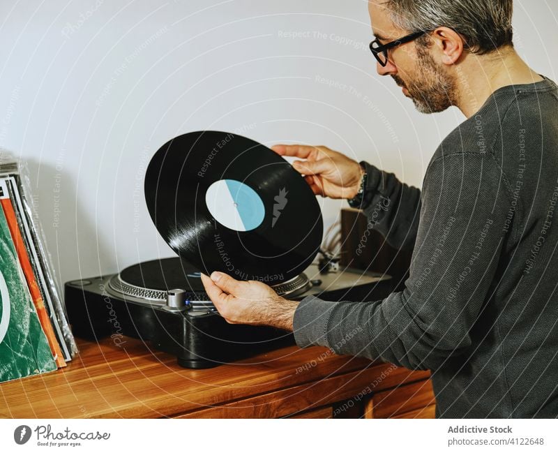 Handsome man listening to music on vinyl record player disc turntable retro vintage nostalgia chill male serious home mature enjoy setting sound song tune