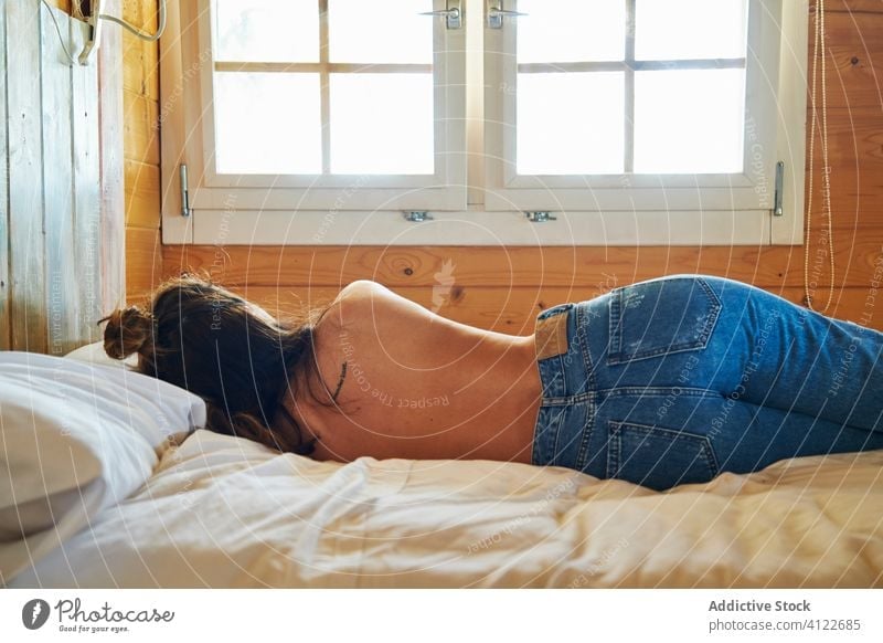 Topless woman lying on bed in morning relax comfort wooden cabinet weekend rest female topless jeans outfit casual cozy tranquil peaceful serene calm lady