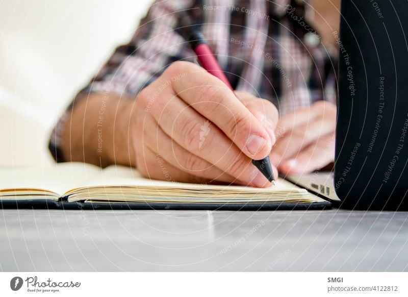 A man writing in a notebook next to a laptop e-learning person education computer online business home technology studying lifestyle internet office homework