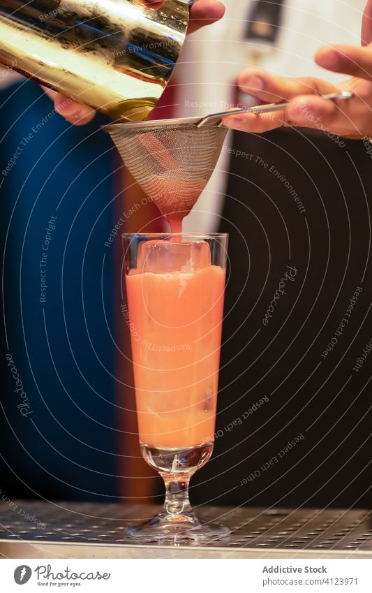 Bartender with sieve pouring cocktail in glass prepare bartender drink alcohol fresh ice barman orange hand counter beverage pub professional cold shaker