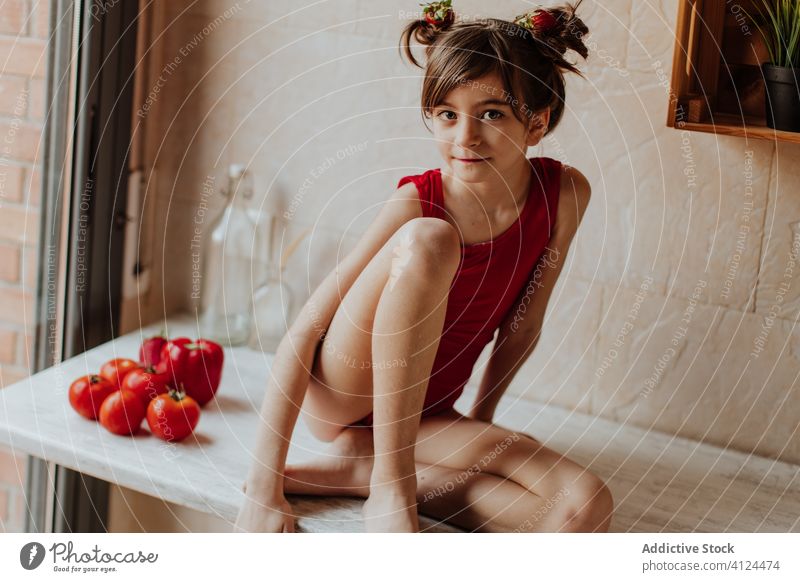 Little girl sitting on counter with tomatoes and red pepper kitchen healthy food bright vegetarian cute barefoot bodysuit home organic vegetables lifestyle