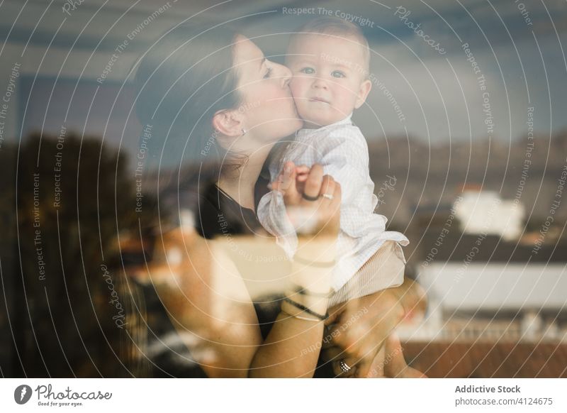 Loving mother hugging and kissing baby love together cute toddler embrace home content outfit window casual happy kid child parent babyhood parenthood childhood
