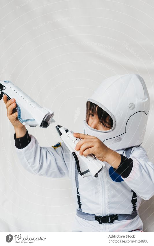 Kid in astronaut costume and helmet playing with toy rockets kid child playful having fun spaceship spacesuit uniform pretend spaceman fantasy dreamy