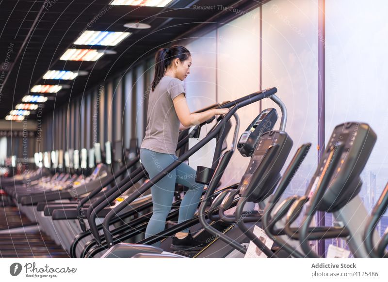 Positive young ethnic sportswoman exercising on machine in modern gym athlete training step cardio cheerful fitness sportswear wellness activity exercise