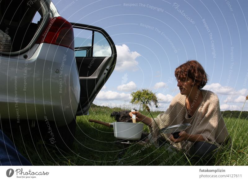 Woman sits in the green next to a car and stirs in a cooking pot boil Trip excursion to the green Freedom trip road trip travel Picnic enjoy nature simple life