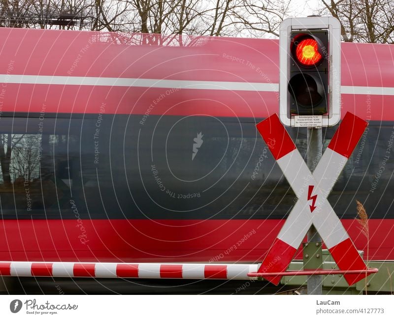 A red train rushes past a closed level crossing with a red-white barrier and red traffic light Railroad crossing Train Train travel Track Control barrier