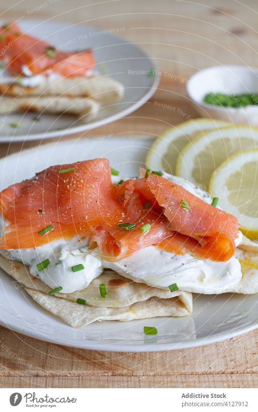 Portions of tasty naan bread with salmon on plates flatbread portion food sour cream green onion table dish garnish sauce fillet wooden meal cuisine delicious