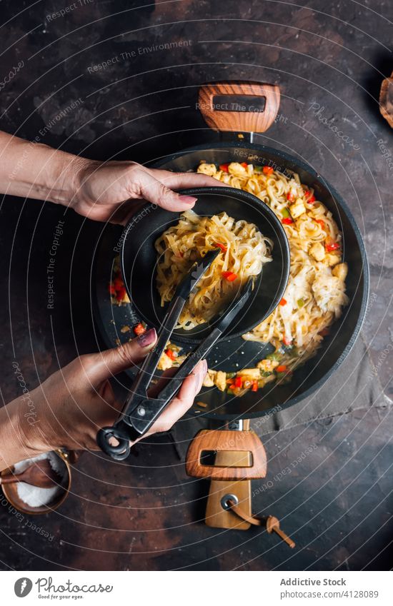 Woman putting stir fry noodles into bowl food serve homemade eat hand take tong spicy chicken dish woman tradition tasty dinner lunch meal delicious asian food