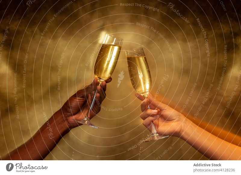 Crop multiracial couple holding wineglasses with champagne on golden background hand party celebrate toast beverage drink alcohol friend together gather cheers