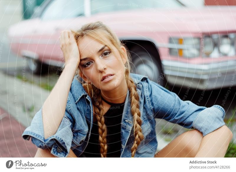 Attractive blonde girl sitting on the sidewalk near to a classic pink car woman young braids old grunge summer portrait leisure urban city outskirts attractive