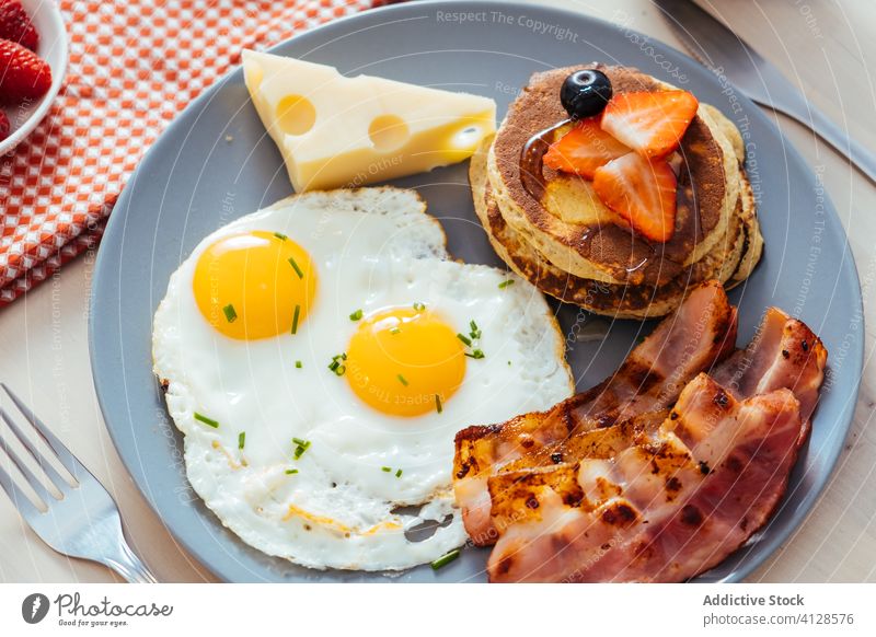 Delicious fried eggs with bacon and cheese for breakfast plate cupcakes strawberries black berries honey food serve meal pancake berry dish table nutrition