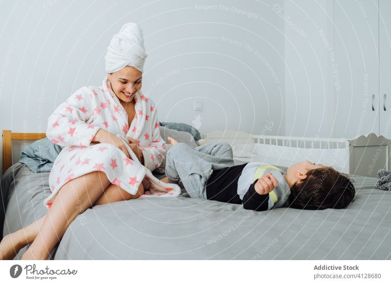 Content mother playing with child in bedroom son having fun together little dressing up game content bathrobe pastime boy parent parenthood mom kid motherhood