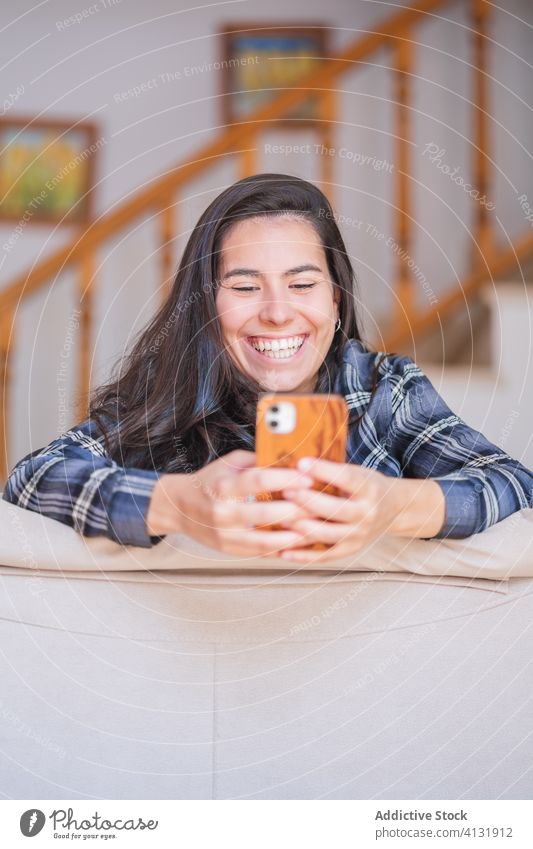 Smiling young woman using smartphone on sofa home happy selfie browsing casual gadget online female lying internet cozy device social media relax couch mobile