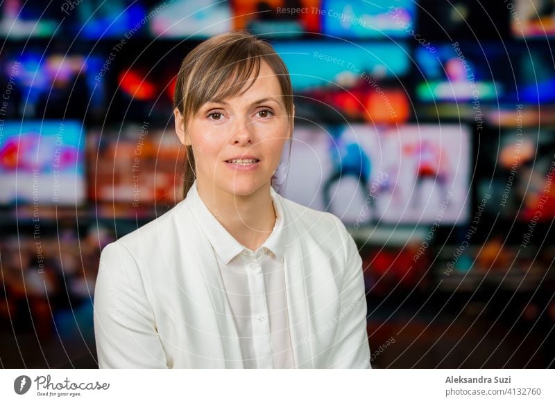 An anchorwoman reporting live breaking news sitting in Tv studio. Background of multiple screens of broadcast control room. Journalism concept announcement