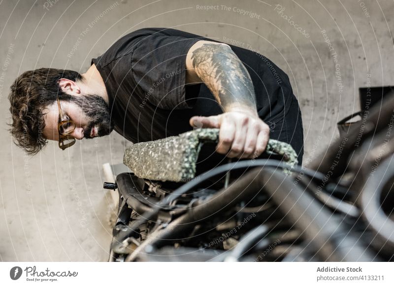 Busy male mechanic repairing motorcycle seat in workshop biker motorbike garage man fix measure transport busy tattoo brutal vehicle maintenance beard grunge