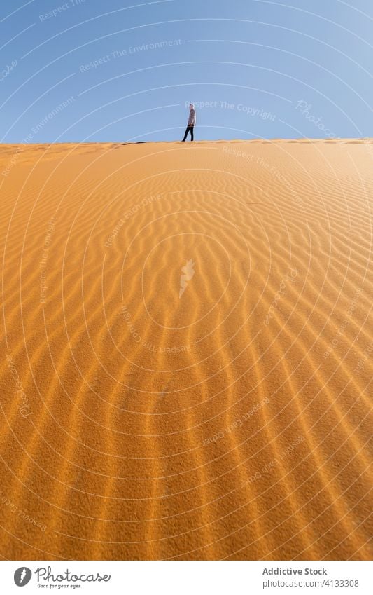 Anonymous traveler walking along sand dune in desert holiday tourist stroll blue sky nature morocco africa terrain sunny summer dry trip landscape adventure