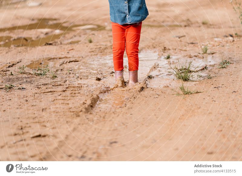 Anonymous curious girl playing in mud puddle child having fun weekend kid rubber boot cute dirty water wet adorable childhood joy activity rest playful ripple