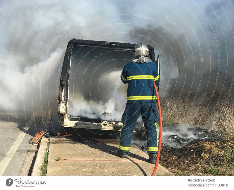 Firefighter putting out fire in car firefighter extinguish fireman put out smoke brave water hose coworker sunny daytime summer energy strong emergency service