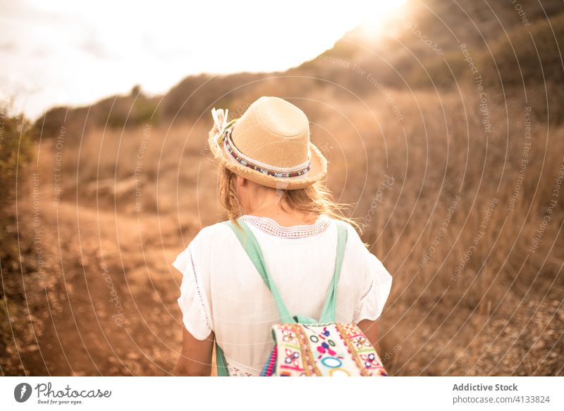 Traveling woman walking along field during sunset hipster traveler vacation mountain summer backpack nature female levanzo island dry grass stroll hat freedom