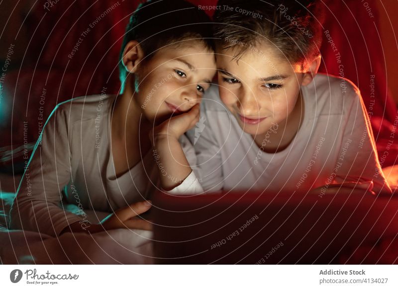 Happy brothers watching video on tablet together cartoon sibling browsing pajama blanket using hide enjoy home daytime interesting positive kid bed boy