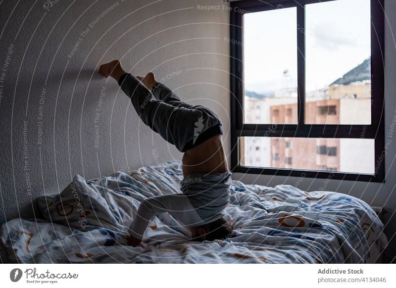 Playful boy performing headstand on bed at home child cute playful pajama having fun weekend kid childhood adorable cheerful happy rest cozy bedroom sleepwear