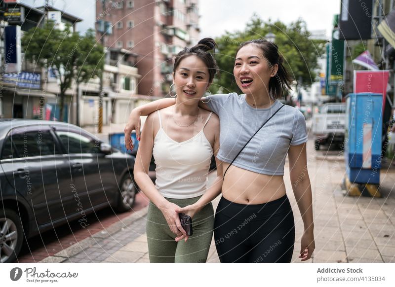 Cheerful ethnic girlfriends walking on street hug happy cheerful shoulder casual slim embrace taipei taiwan together stroll lifestyle smile young urban joy city
