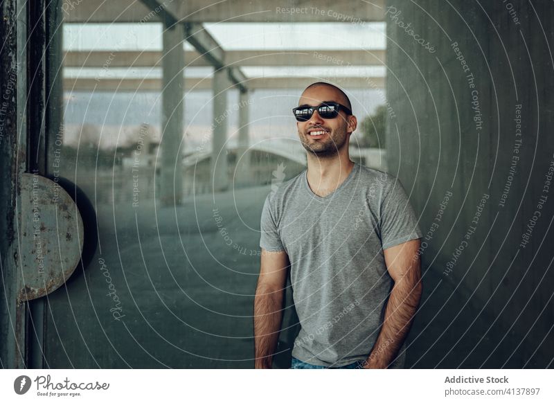 Young man in stylish clothes standing near weathered building young hipster style wall shabby happy confident modern thoughtful male handsome guy casual alone